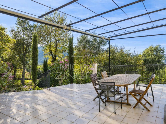 Terrasse ensoleillée avec table en bois et chaises, entourée de verdure à Mandelieu-la-Napoule.
