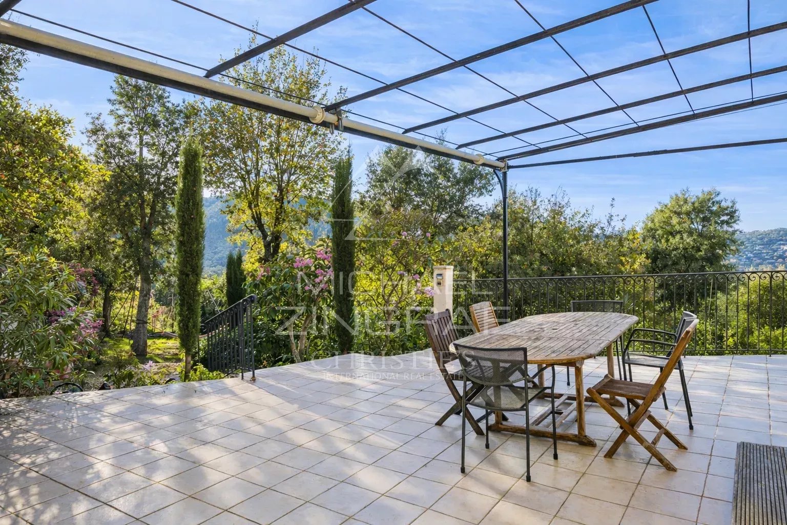 Terrasse ensoleillée avec table en bois et chaises, entourée de verdure à Mandelieu-la-Napoule.