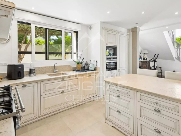 Interior of a spacious and bright kitchen with white furniture and windows overlooking the outside.