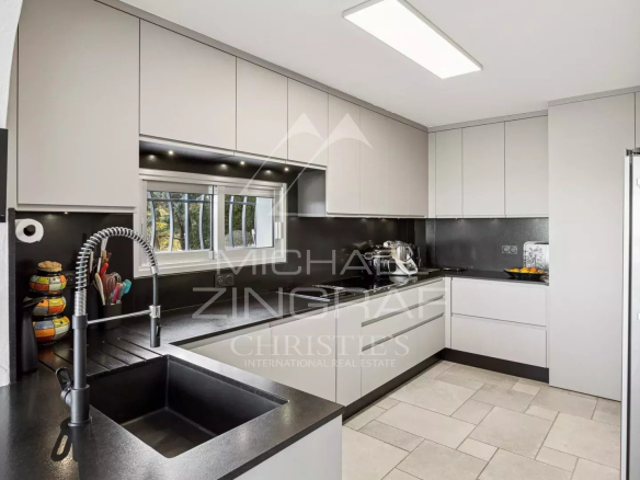 Modern kitchen with black worktops and light-colored furniture, view of the outside.