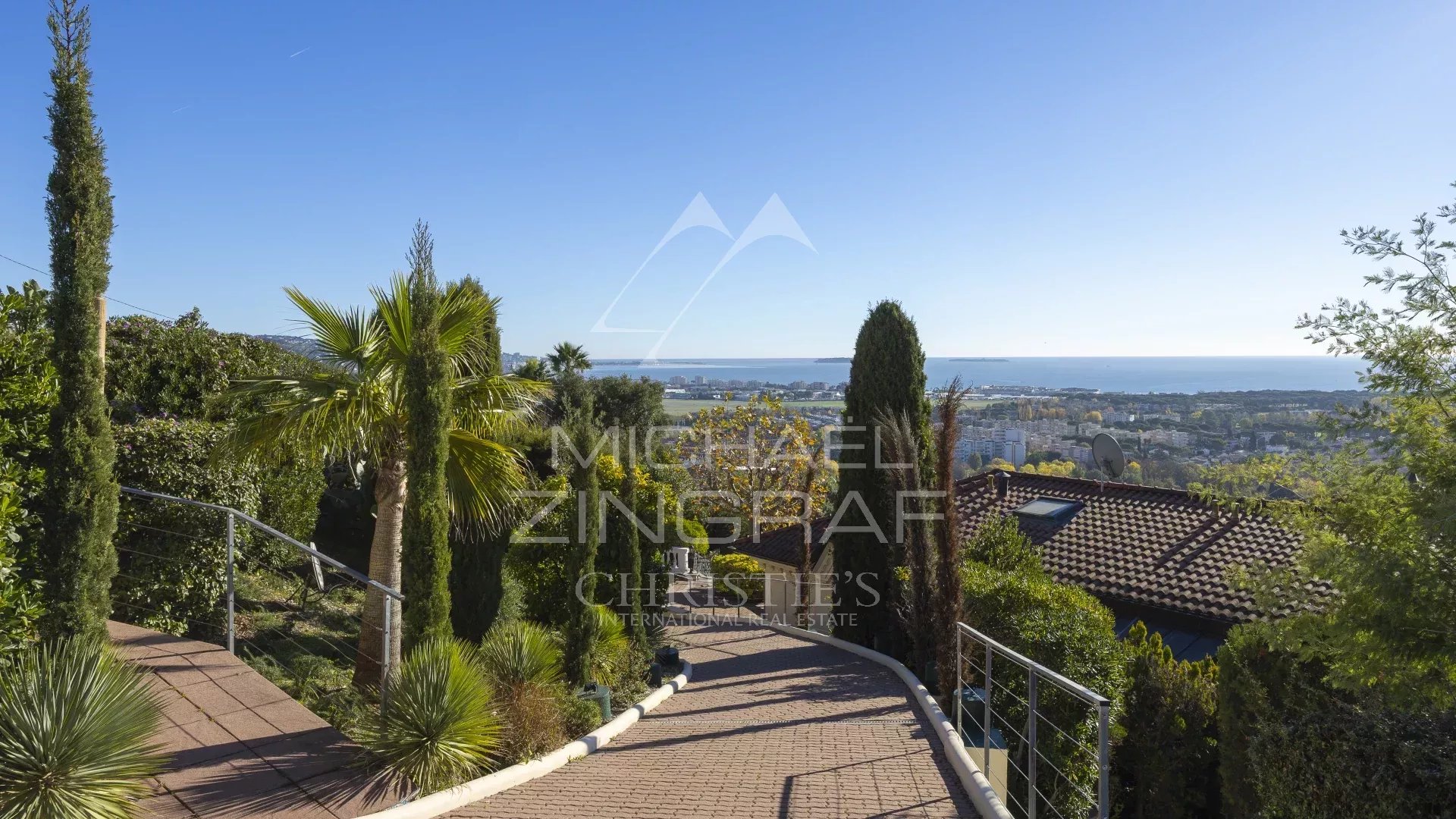 Villa with sea view in Mandelieu-la-Napoule Unobstructed sea view from a hill in Mandelieu-la-Napoule, with palm trees and houses.