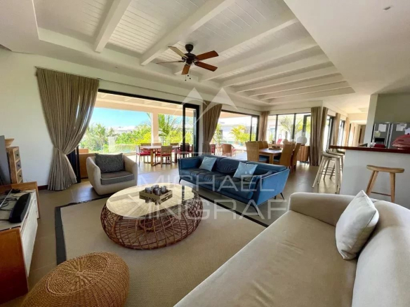 Open-plan living room with a white coffered ceiling, ceiling fan, and large glass doors opening to a patio; beige sofa, blue loveseat, and round wicker coffee table.