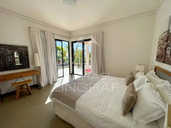 Bright bedroom with a large bed, white bedding and beige pillows, near glass doors to an outdoor patio.