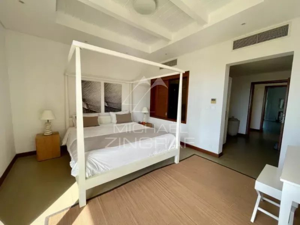 Bright hotel bedroom with a white four-poster bed, two nightstands with lamps, and a beige rug.