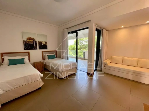 Hotel room with two single beds, teal pillows, and a beige sofa near a balcony door.