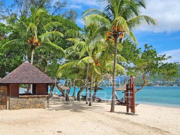 Tropical beach scene with stone cabanas, palm trees, and calm turquoise water, mountain in the distance