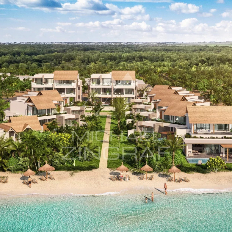 Luxurious beachfront resort with villa-style buildings among palm trees along a sandy shore and turquoise sea far from a forested hinterland, sunny sky.
