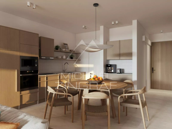 Open-plan kitchen and dining area with wooden cabinets, a round dining table, and six woven chairs; fruit bowl centerpiece. Best for an interior room photo.