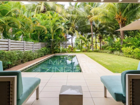 Rectangular backyard pool surrounded by tiled patio, two turquoise lounge chairs, and lush tropical plants and palm trees.