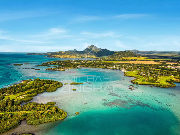 Aerial view of a tropical coastline with turquoise lagoons, green islands, and a small village along the shore, with mountains in the distance.