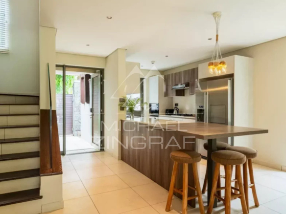 Open-plan kitchen with a wooden island and three bar stools, stairs to the left, glass doors to outdoors.