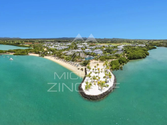 Aerial view of a tropical resort on a curved sandy peninsula with palm trees, turquoise water, and white buildings in the background.