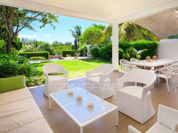 White outdoor patio with wicker seating and glass coffee table, green lawn and palm trees beyond. (informative)
