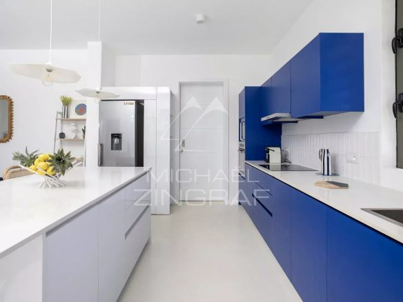 Bright modern kitchen with a white island, blue cabinets, a stainless fridge, and a fruit bowl on the counter.