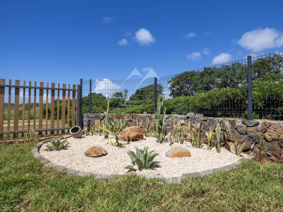 Rock garden with gravel, succulents, and large decorative stones behind a metal and wooden fence under a blue sky.