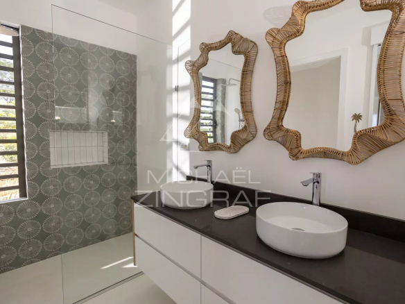 Double vanity with two white vessel sinks on a dark countertop and irregular woven mirrors above.