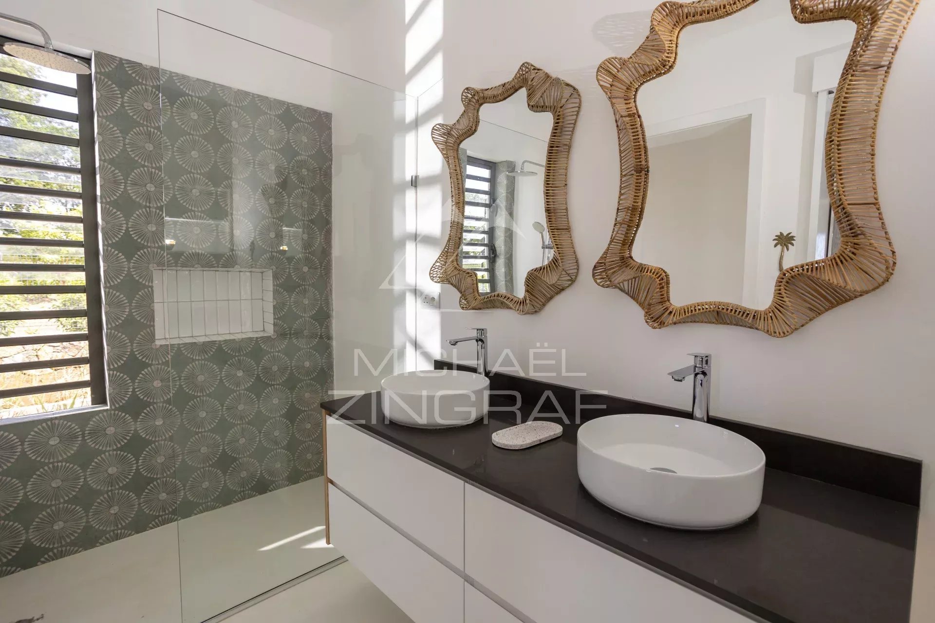 Double vanity with two white vessel sinks on a dark countertop and irregular woven mirrors above.