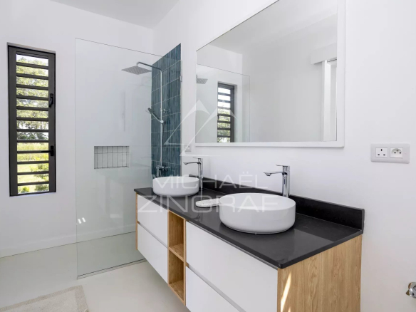Modern bathroom with double vessel sinks on a black countertop and a large frameless mirror above a white-and-wood vanity.