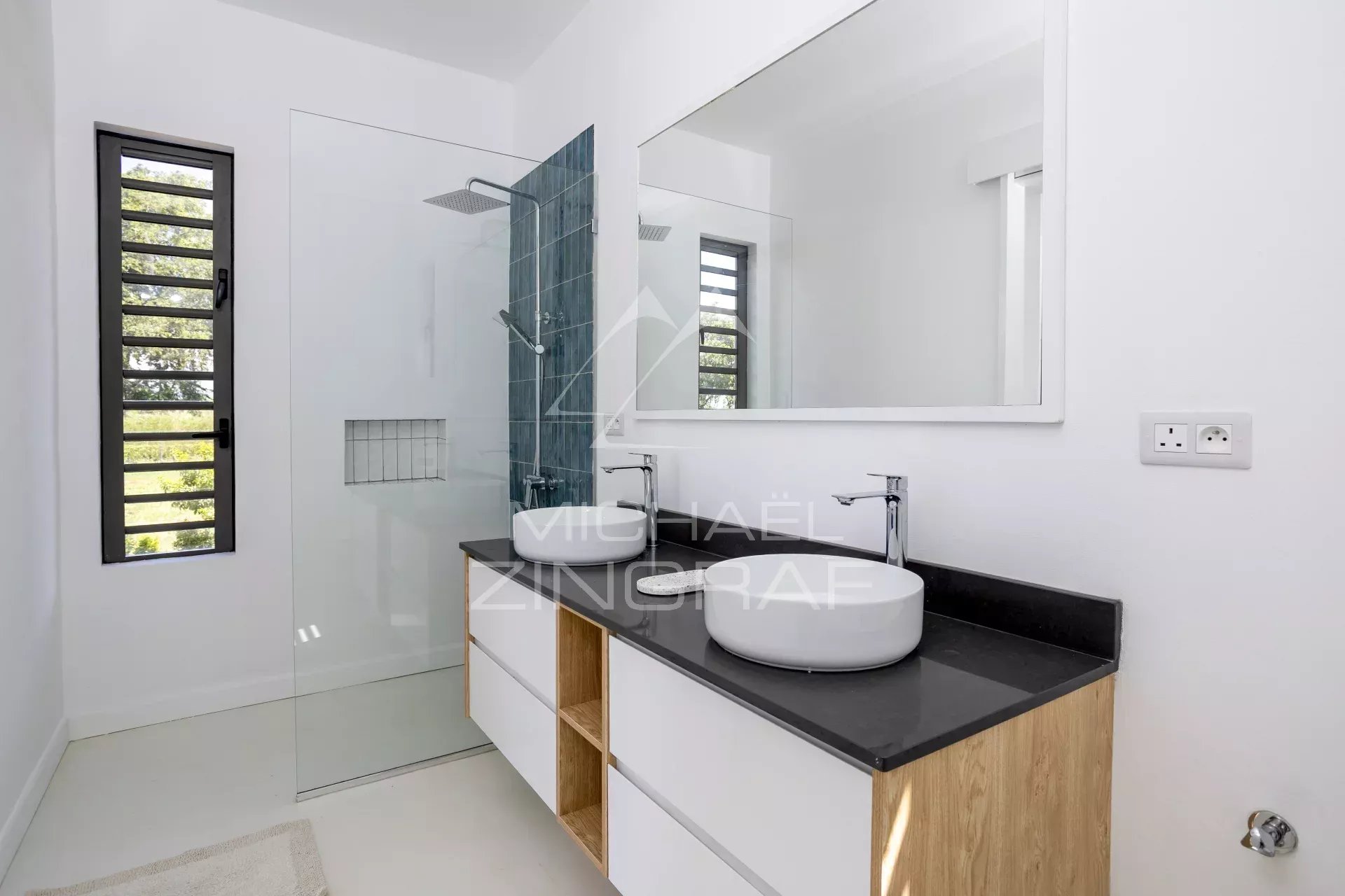 Modern bathroom with double vessel sinks on a black countertop and a large frameless mirror above a white-and-wood vanity.