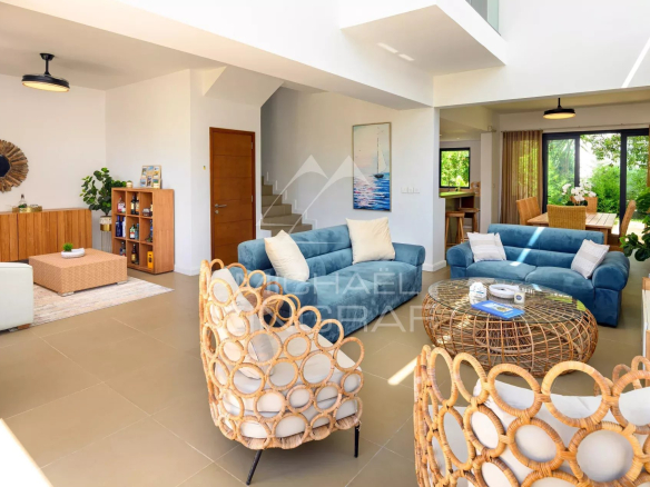 Bright open-concept living room with blue sofas, wicker chairs, and a round wicker coffee table in a sunlit space.