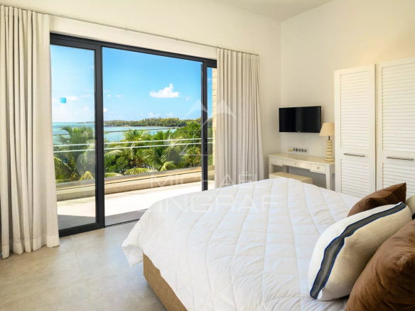 Bedroom with a white quilted bed facing a sliding glass door to a balcony and tropical ocean view.