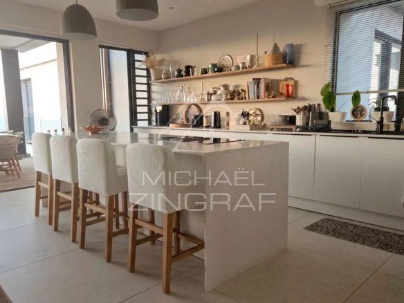 Intérieur d'un penthouse moderne avec cuisine ouverte et bar, vue sur la mer en arrière-plan.