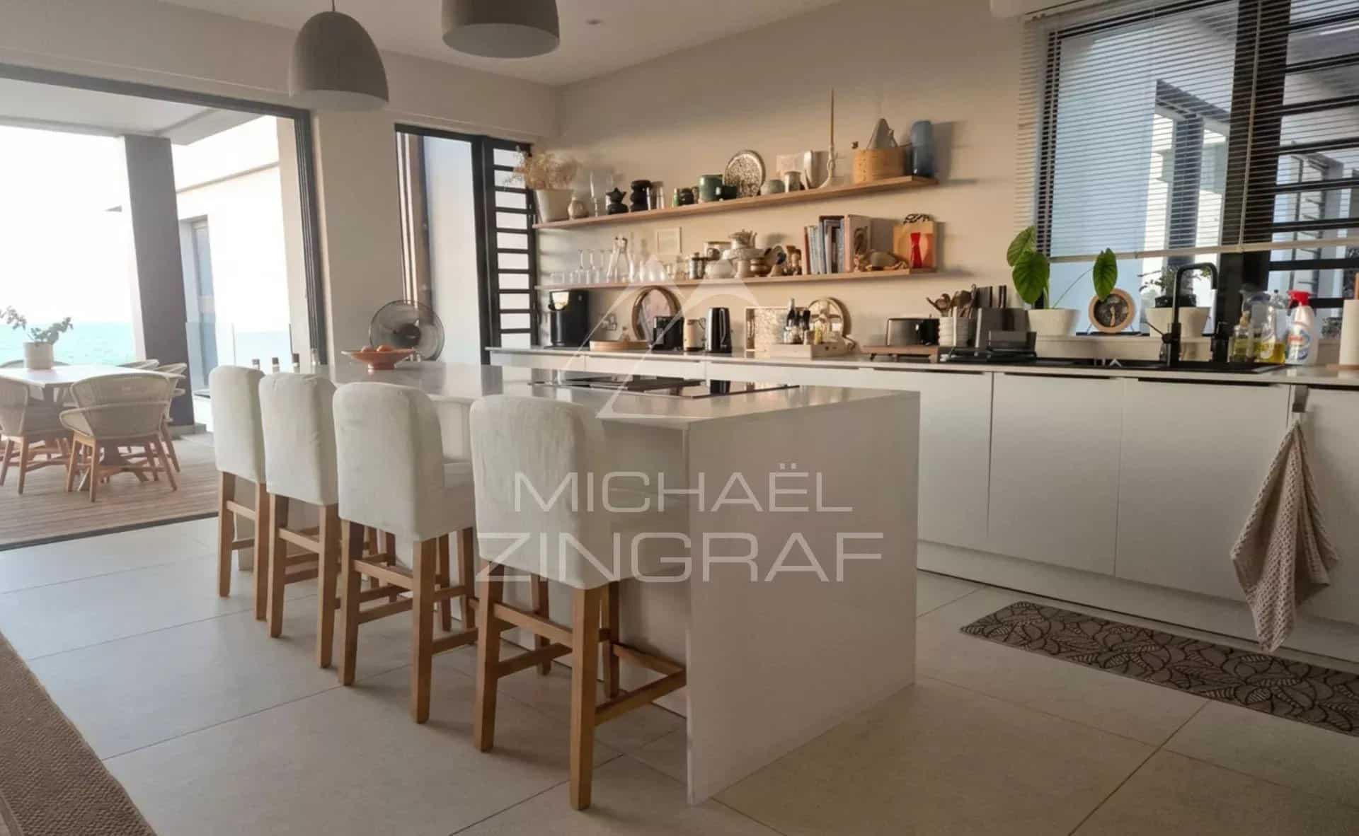Intérieur d'un penthouse moderne avec cuisine ouverte et bar, vue sur la mer en arrière-plan.
