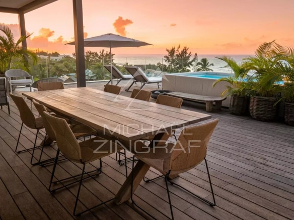Terrasse d'un penthouse avec vue sur la mer au coucher de soleil, mobilier moderne en bois et chaises en métal.