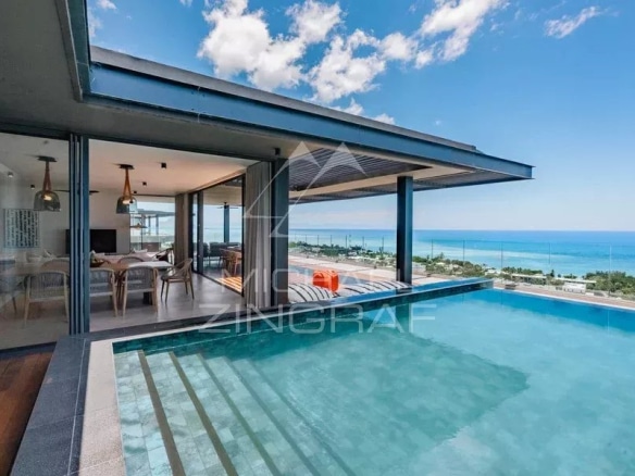 Vue de la piscine à débordement d'une villa moderne avec terrasse surplombant la mer.