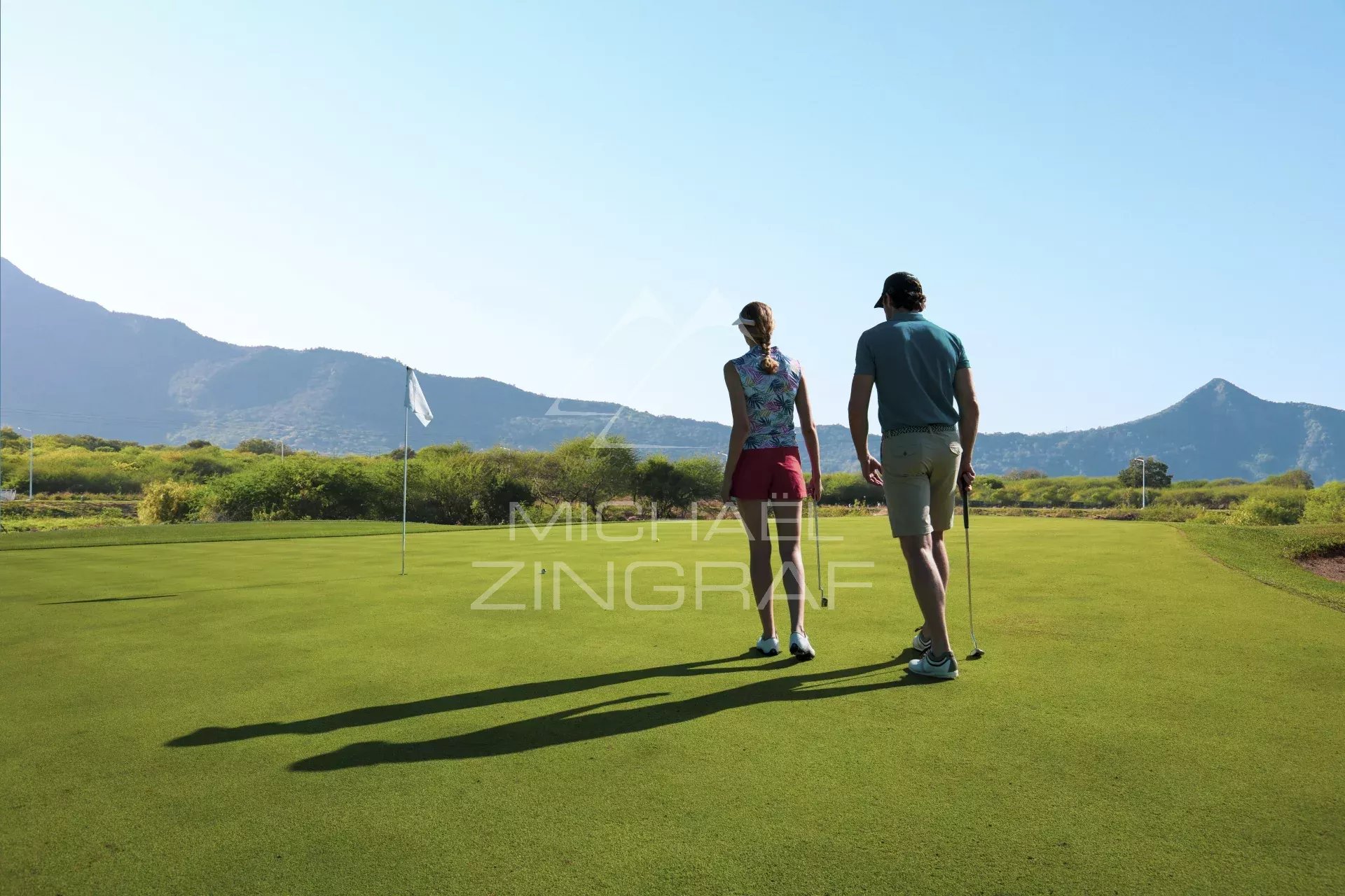 Deux personnes sur un green de golf avec des montagnes en arrière-plan à Rivière Noire, Île Maurice.