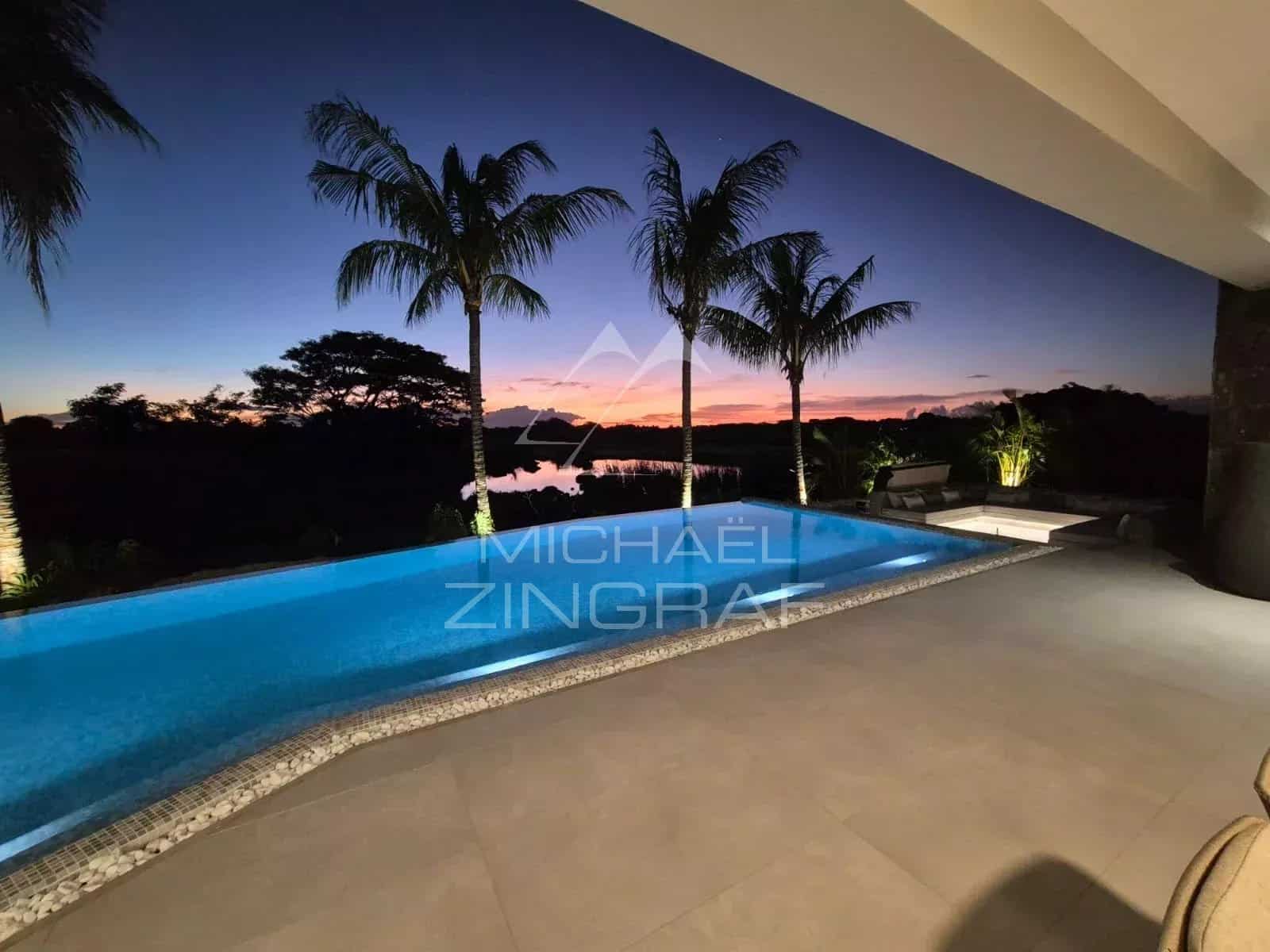 View of a contemporary villa with a swimming pool at sunset, surrounded by palm trees.