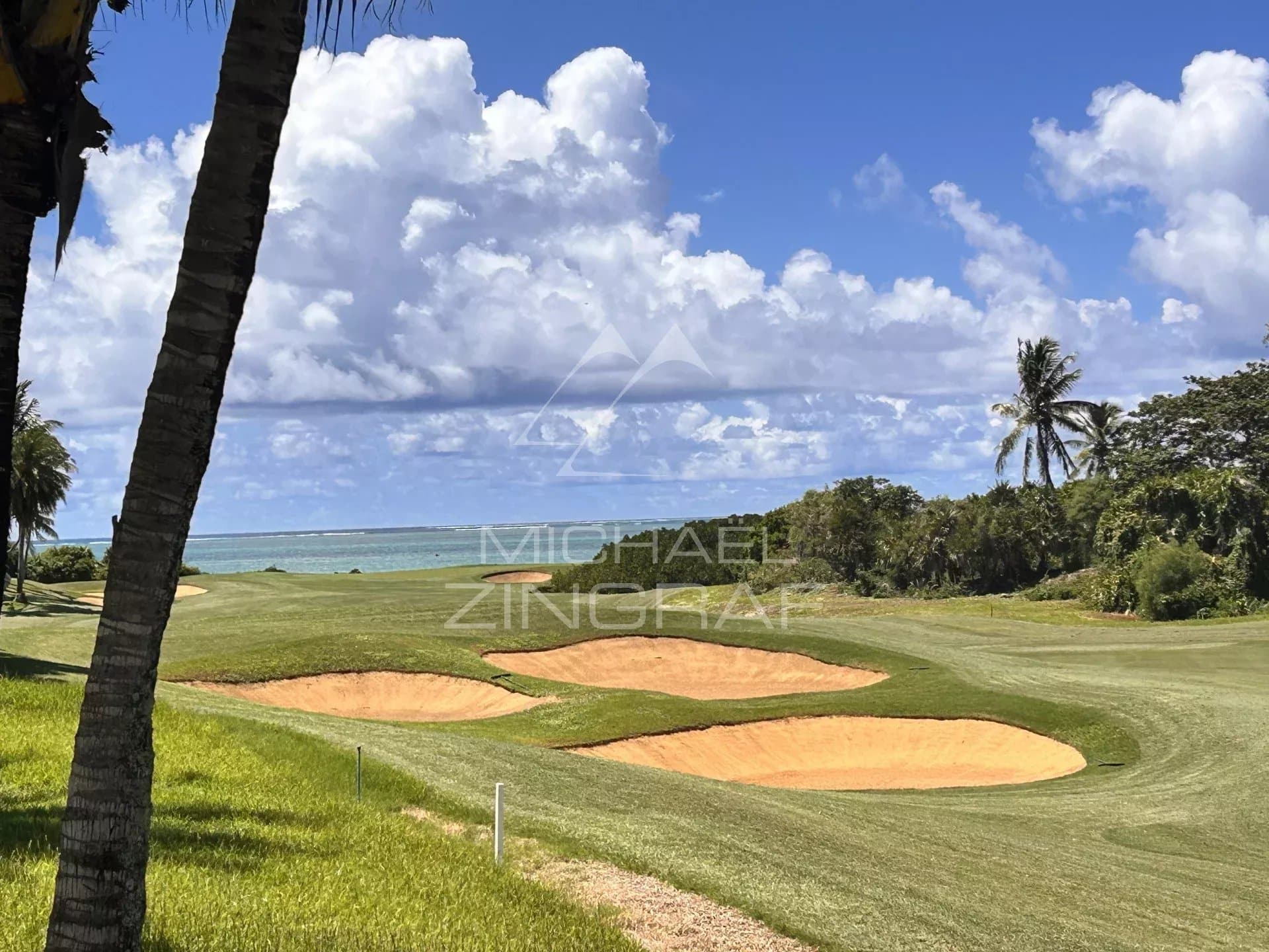 View of a golf course with bunkers and a lagoon in the background at Beau Champ.