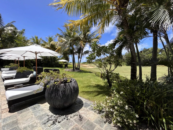 View of the villa with swimming pool, sun loungers and palm trees, overlooking a golf course.