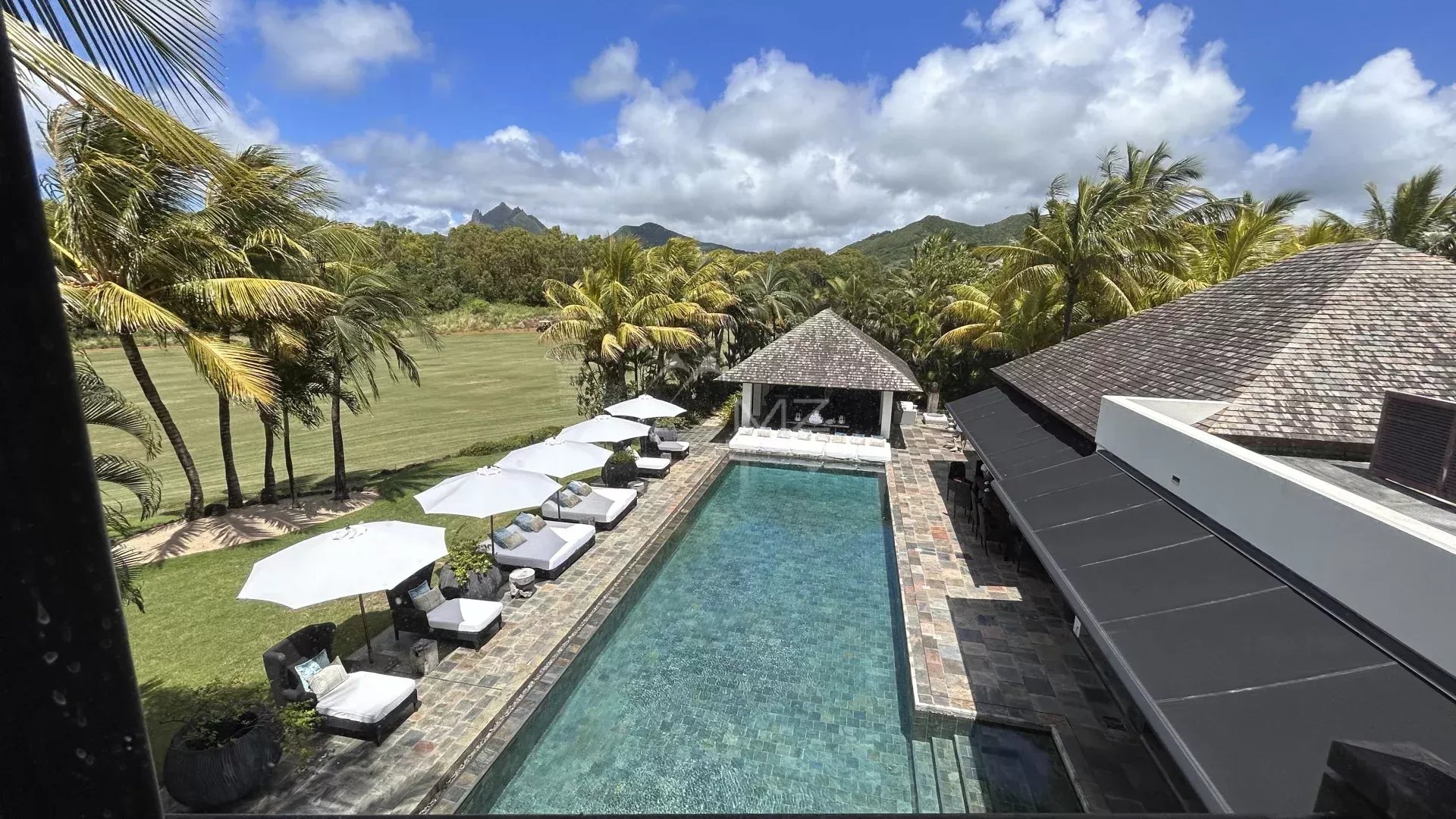 View of a villa with swimming pool and sun loungers, surrounded by palm trees and a golf course.