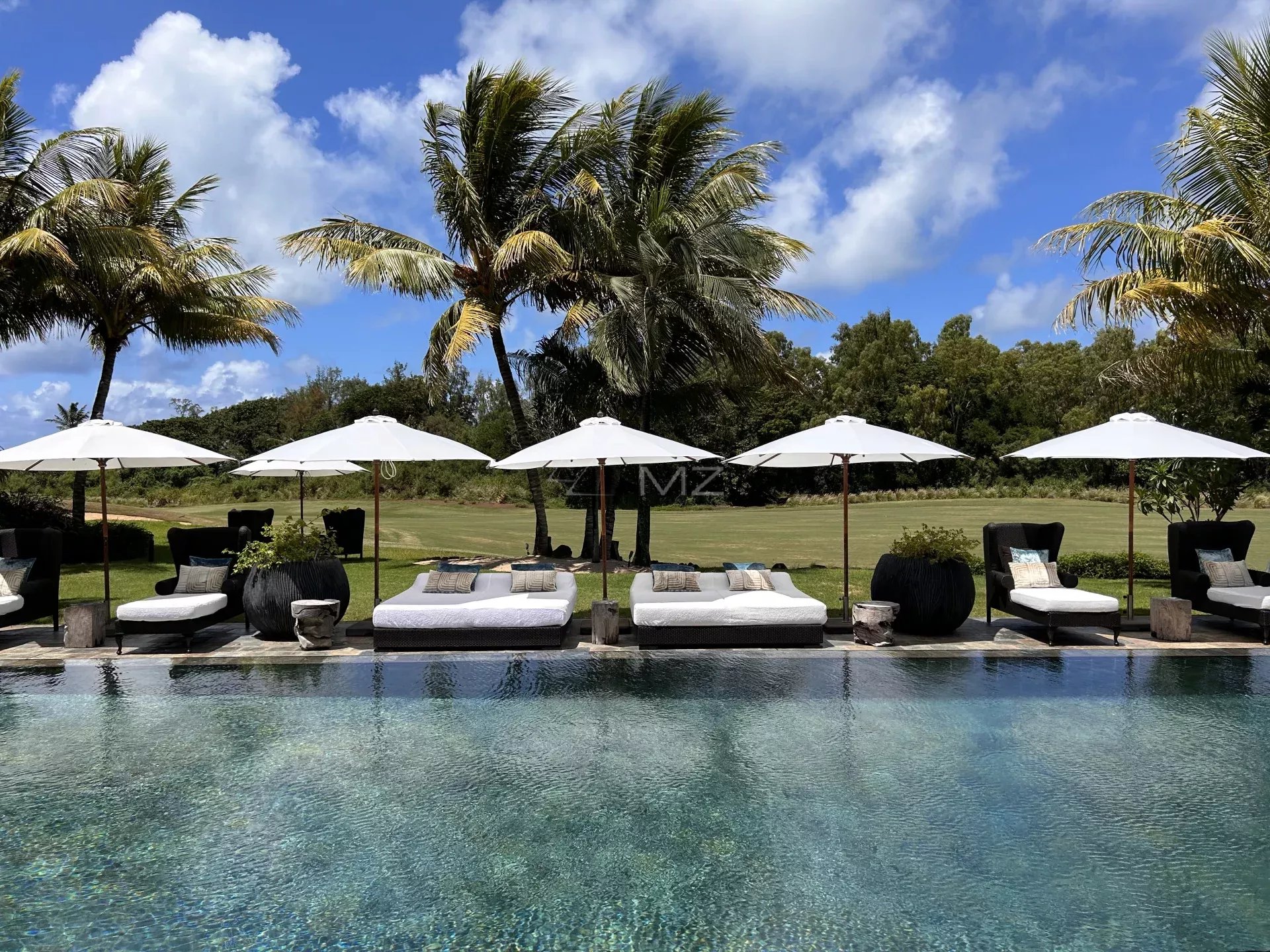 View from the swimming pool of a villa with sun loungers and parasols, surrounded by greenery and a golf course in Beau Champ.
