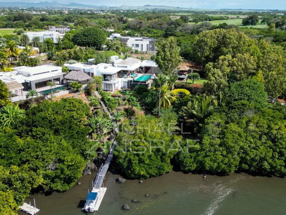 Vue aérienne d'une villa de luxe avec piscine et jardin, située près d'un lagon et d'un golf.