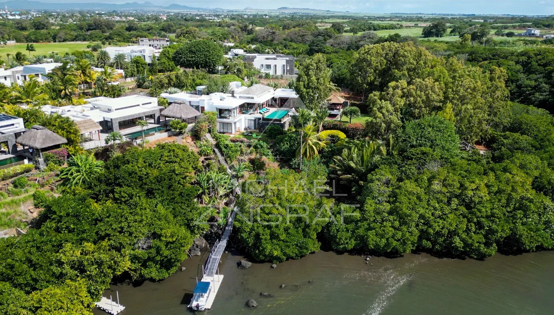 Vue aérienne d'une villa de luxe avec piscine et jardin, située près d'un lagon et d'un golf.