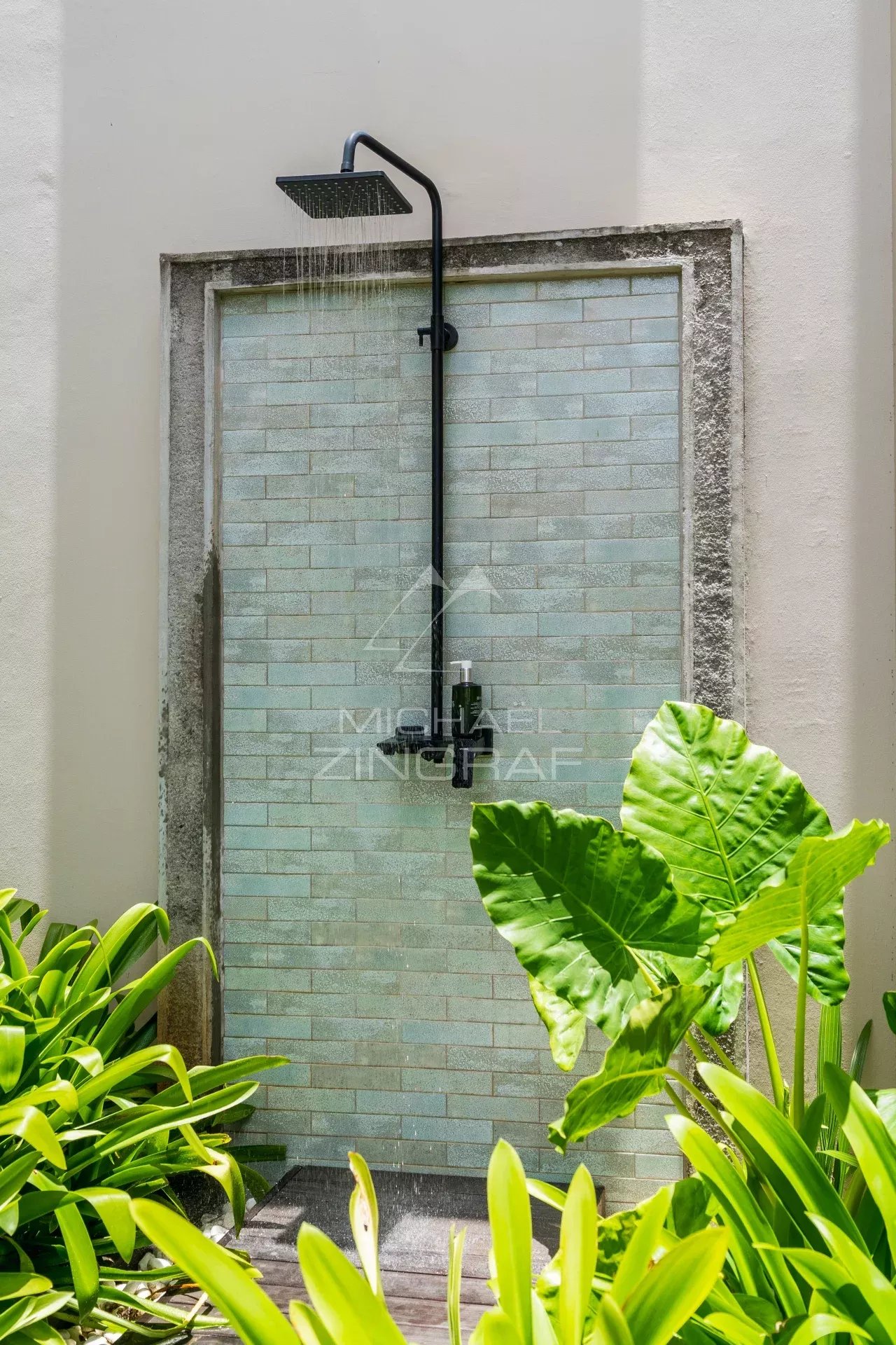 Douche extérieure moderne entourée de plantes vertes.