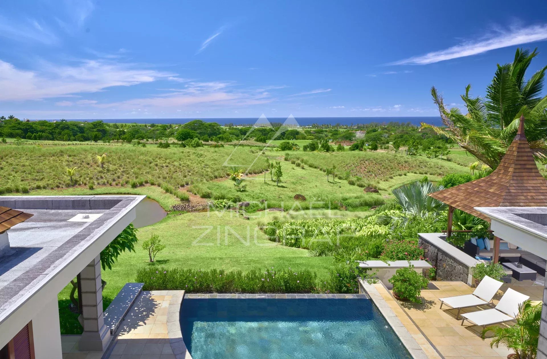 View of a villa with a swimming pool overlooking a golf course, surrounded by greenery and the ocean in Bel Ombre, Mauritius.