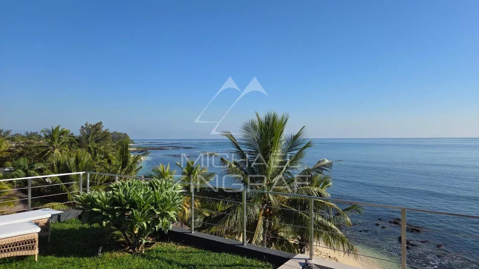 Ocean view from a terrace with palm trees and green space.
