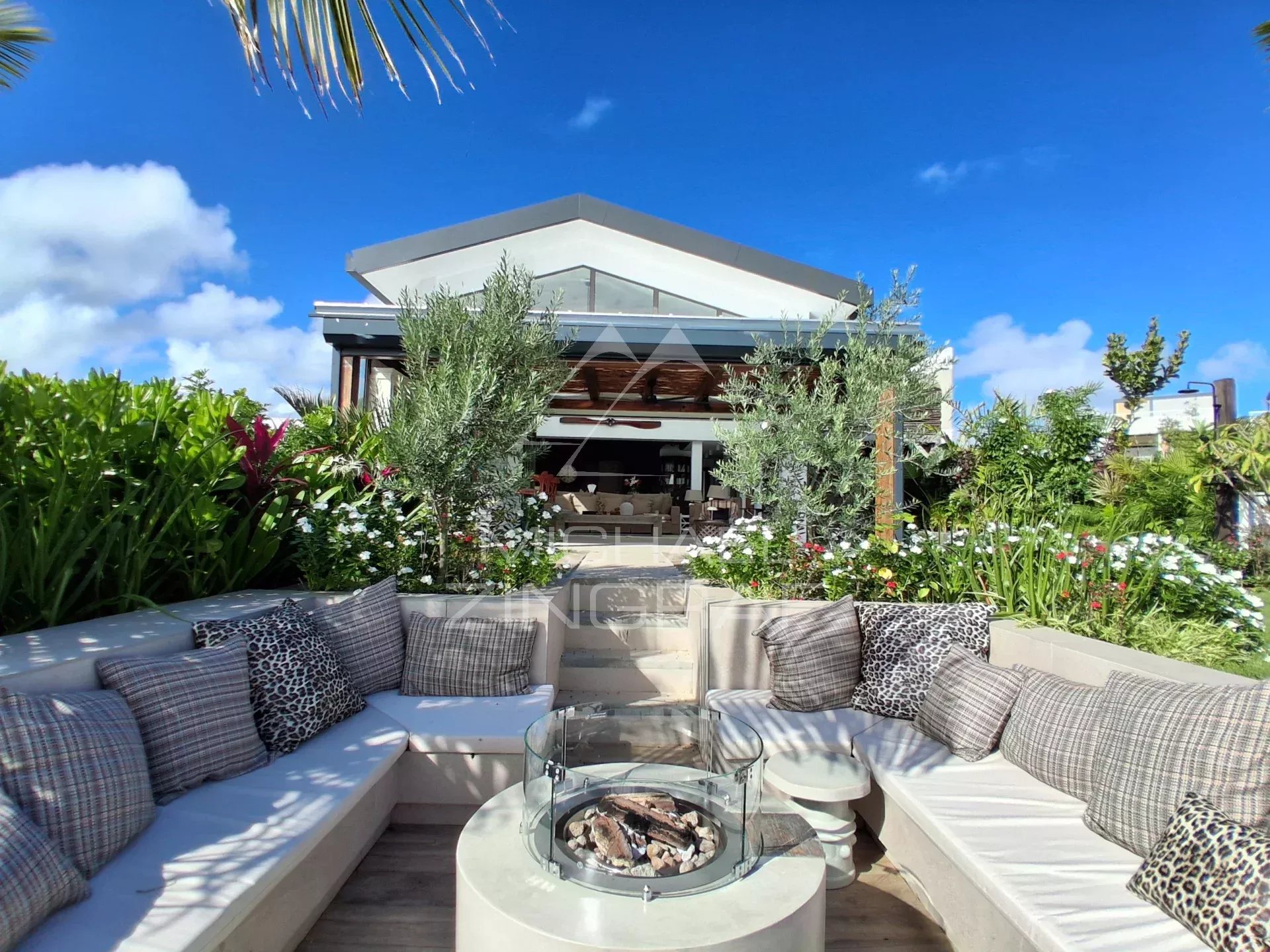 Terrace of an apartment in Pointe aux Canonniers with a view of the lagoon, comfortable furniture and a flower garden.