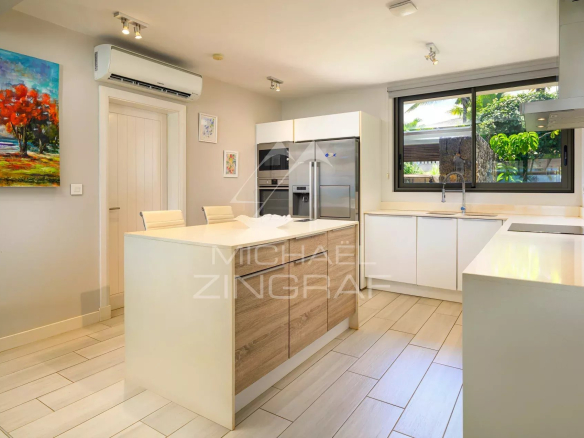 Cuisine moderne avec îlot central et appareils électroménagers en inox dans une villa à Haute Rive.