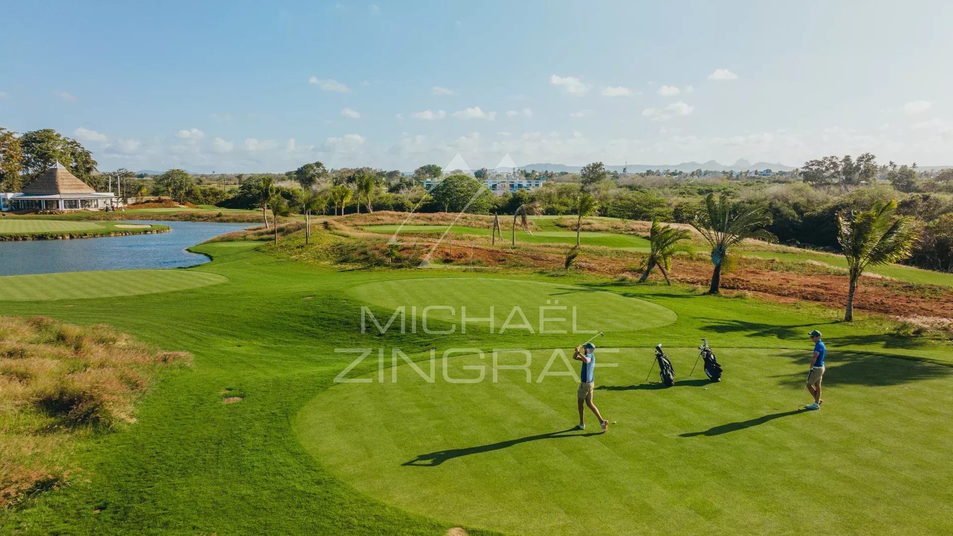 Parcours de golf à Haute Rive Un golfeur sur un parcours verdoyant avec des palmiers et un plan d'eau en arrière-plan.