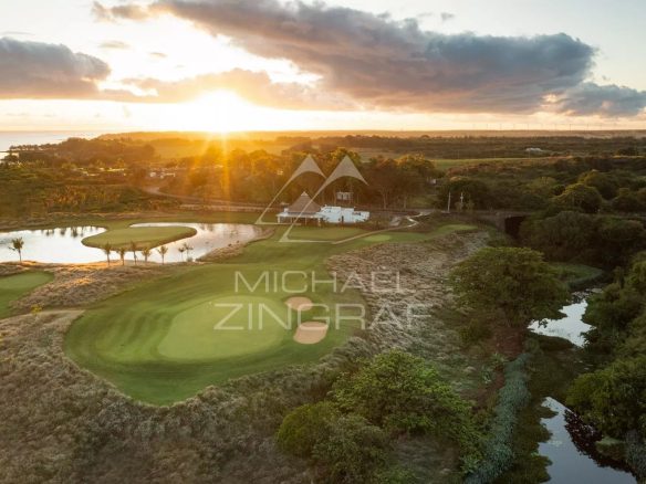 Panoramic view of a golf course at sunset, with trees and water.