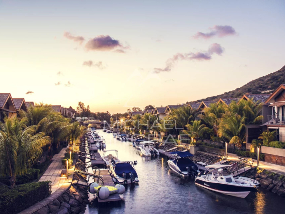 Vue de La Balise Marina avec des bateaux amarrés et des maisons en bord de canal au coucher du soleil.