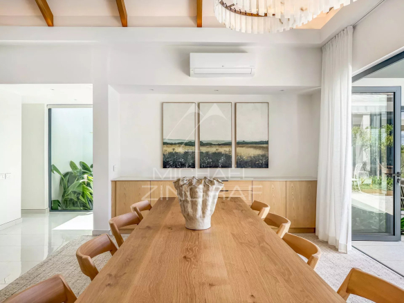 Salle à manger d'une villa moderne avec une grande table en bois et des œuvres d'art au mur.
