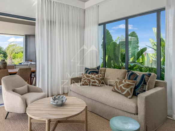 Intérieur d'une villa moderne avec un salon lumineux, des fenêtres grandes et des plantes vertes à l'extérieur.