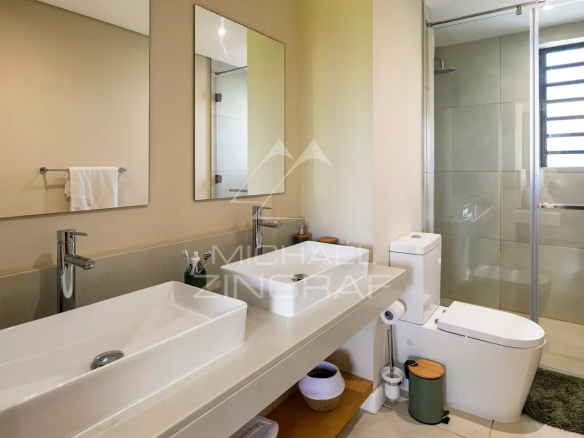 Salle de bain moderne avec lavabo, miroir et douche dans une villa à Azuri, Haute Rive.