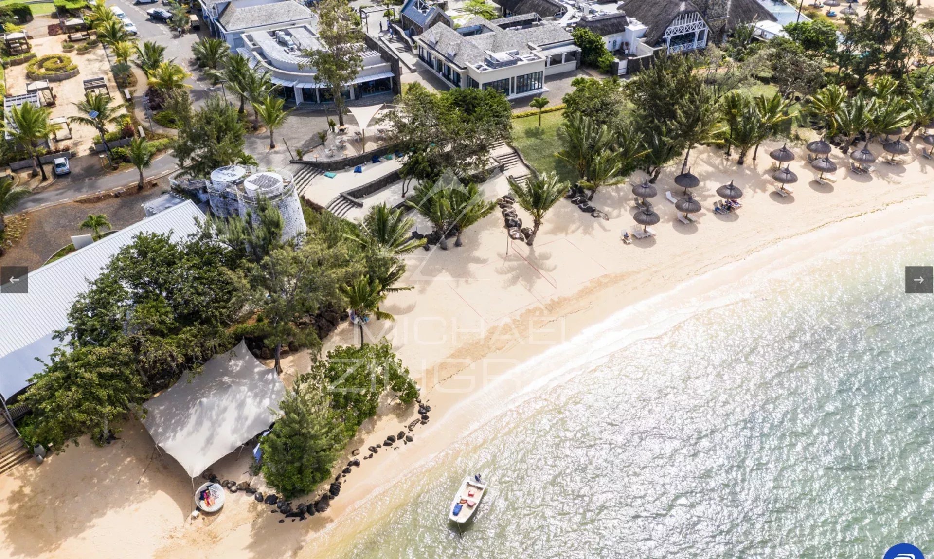 Vue aérienne d'une plage avec des parasols et des bâtiments en bord de mer.