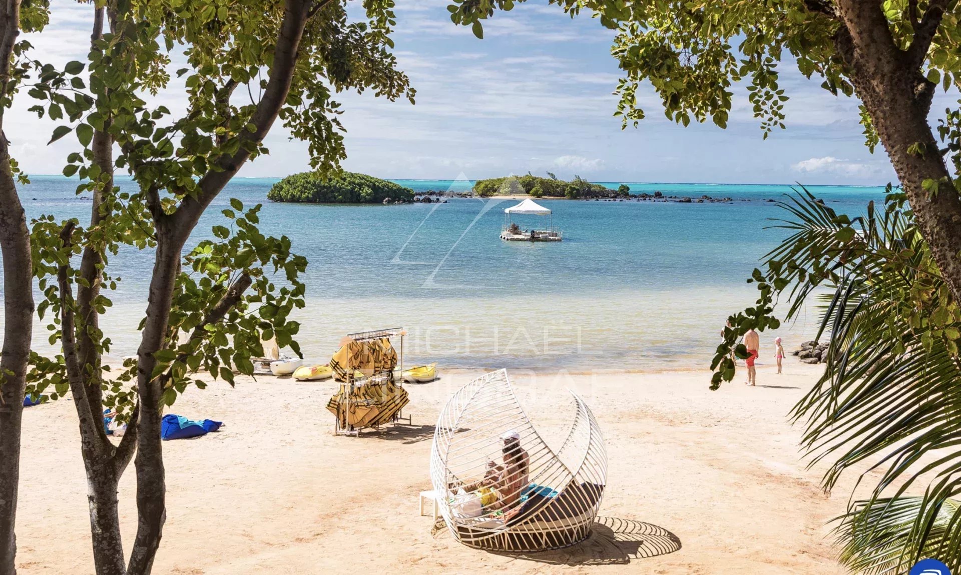 Plage avec vue sur l'eau et îlots, chaises longues et un bateau au loin.